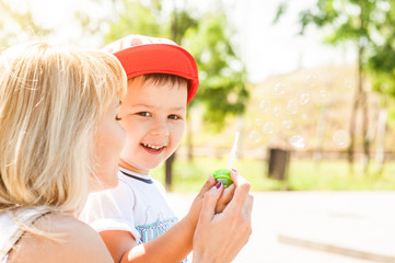 Wall Mural - Mother and son playing together outdoors in park with soap bubbles