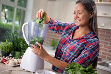 Wall Mural - young woman with blender chopping green vegetables for detox sha