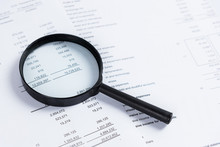 Magnifying Glass On Financial Statement Paper. Analyzing Business Financial Data.