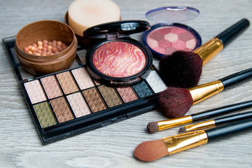 Set of decorative cosmetics and brushes on grey wooden background. Various browns makeup products. Close up.