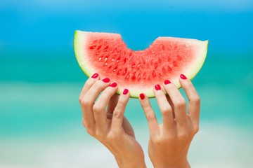 Wall Mural - Hand holding slice of watermelon on the beach. 