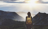 Fototapeta  - Hipster young girl with bright backpack enjoying sunset on peak of foggy mountain. Tourist traveler on background valley landscape view mockup. Hiker looking sunlight flare in trip in northern spain