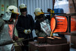© Connect Images - Male foundry workers pouring bronze melting pot in bronze foundry