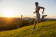 Bare chested man running on meadow in park at sunset
