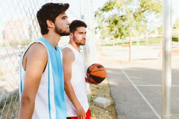 Portrait of two friends relaxing after playing basketball on court.