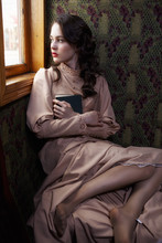 Young Woman In Beige Vintage Dress Of Early 20th Century Sitting