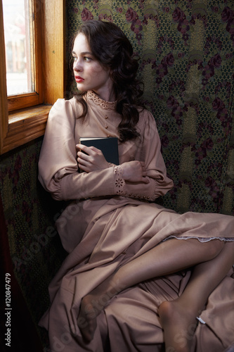 Young woman in beige vintage dress of early 20th century sitting