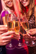 © pressmaster - A close up of five hands clinking glasses with champagne, two girls are in the backgrounds