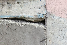 Texture Of A Concrete Wall With Cracks And The Remnants Of A Pink And Blue Paint.
