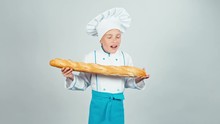 Cute Happy Baker Girl Child Sniffing Bread Baguette Isolated On White And Smiling At Camera
