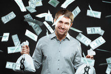 Happy Man Holding Money Bags Looking At Camera With Money Falling Behind