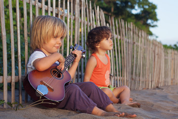 Little happy boy have fun, play music on Hawaiian guitar ukulele for small baby girl, enjoying sunset ocean beach. Children healthy lifestyle. Travel, family activity on tropical island summer holiday