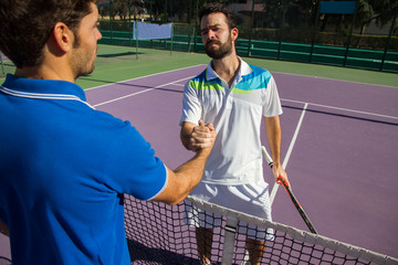 Wall Mural - Two men, professional tennis players shake hands before and after the tennis match. One of they has the face of anger. He is trying to intimidate his opponent. 