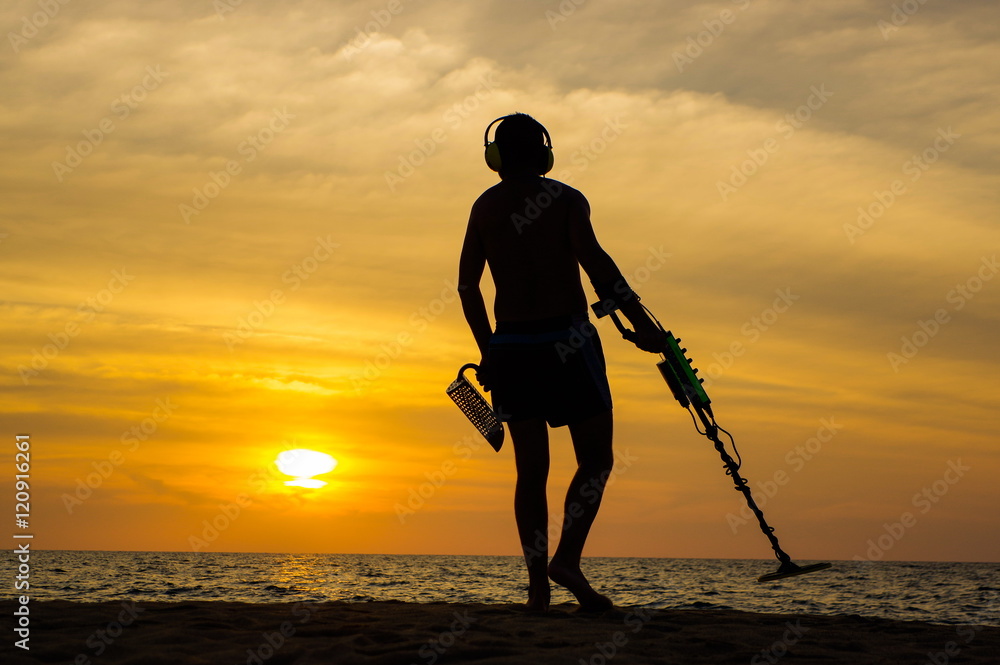 a treasure hunter with Metal detector on sunset on the beach - obrazy, fototapety, plakaty 