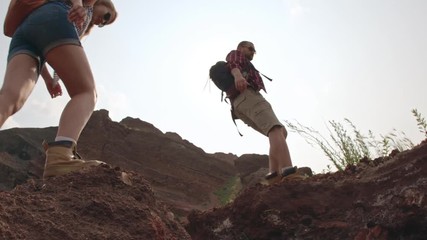 low angle shot of boyfriend and girlfriend with backpacks jumping over precipice on hiking trip