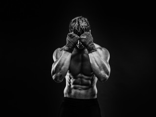 Unrecognizable topless man in fighting gloves covering face with fists on black background. Isolate.