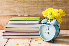 Heart Shape Retro Clock On Wooden Floor With Yellow Flower In White Pot And Old Books.