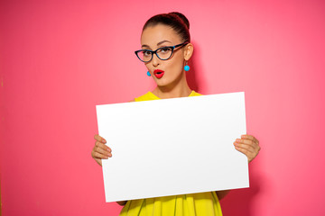 Your text here. Pretty young excited woman holding empty blank board. Colorful studio portrait with pink background.