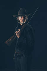 Retro 1900 western cowboy standing with rifle. Young man. Studio