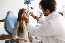 Male Optometrist With Trial Frame Checking Patient Vision At Eye Clinic 