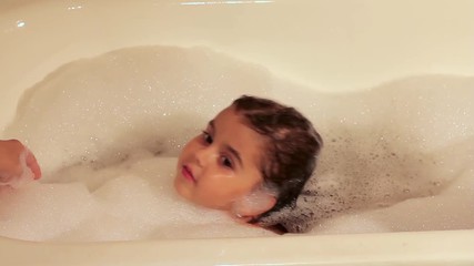 curly girl bathes in a bath with foam. learn to swim. water treatments.