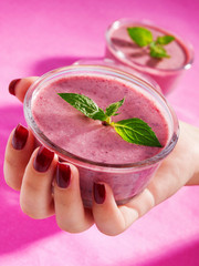 Female hand holding raspberry cream with mint shot on pink backg