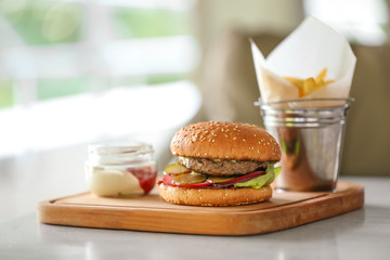 Canvas Print - Tasty burger with french fries and sauce on wooden cutting board