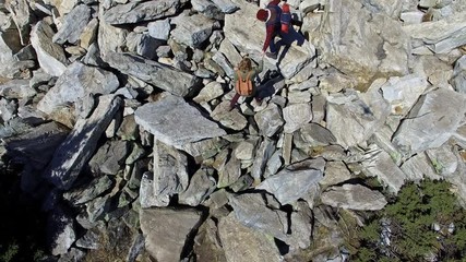 aerial with tilt up of boyfriend and girlfriend climbing on enormous rocky mound