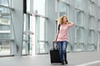 © mimagephotos - Happy young woman walking with suitcase and cell phone