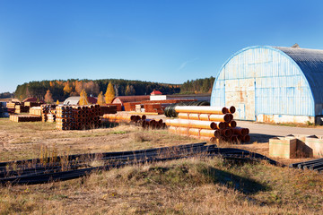 landscape of metal round warehouse and pvc orange plastic pipe stacks for plumbing in front the autumn forest