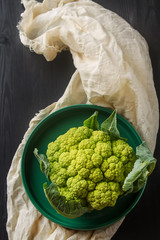 Ripe green cauliflower on a plate, light fabric. Dark wood backg