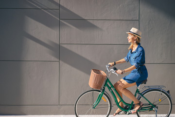 Wall Mural - Cycling lifestyle. Pretty young woman in hat riding bicycle against grey wall.