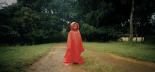 Portrait Of A Young Girl Wearing A Red Hooded Cape Outdoors.