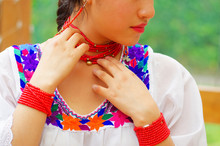 Closeup Beautiful Hispanic Woman Wearing Traditional Andean White Blouse With Colorful Decoration Around Neck, Matching Red Necklace, Bracelet And Ear Ring