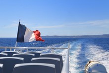 French Tricolour Flag Flying On The Back Of A Boat Leaving A Wake Through The Blue Mediterranean Sea In Summer