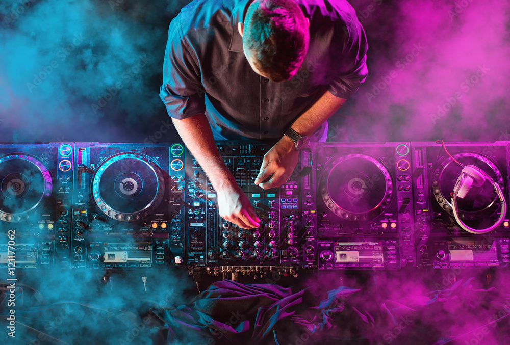 Charismatic disc jockey at the turntable. DJ plays on the best, famous CD players at nightclub during party. EDM, party concept. - obrazy, fototapety, plakaty 