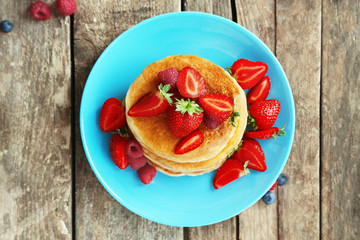 Wall Mural - Tasty pancakes with fresh berries on plate on wooden background, top view