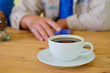 © sarawutnirothon - White coffee cup on wooden table with blurred man background.
