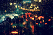 City View Through A Window On A Rainy Night,Rain Drops On Window With Road Light Bokeh, City Life In Night In Rainy Season Abstract Background.