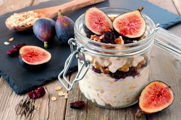 Wall Mural - jar of overnight autumn oats with red figs, cranberries and walnuts against a rustic wood background
