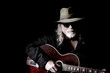 © Perry Correll - Middle-aged Caucasian man with long hair and a white beard wearing sunglasses, a hat and black shirt while holding a guitar. Black background and sidelighting. Vintage filter and desaturation applied