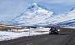 A local driving a red car on Iceland Ring Road with snow-capped mountain in the back ground.