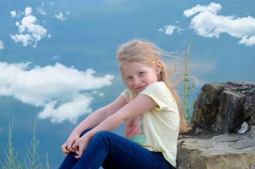 caucasian blonde little girl on top of the mountain, blue sky and clouds
