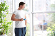 © Africa Studio - Handsome man standing near window with cup of morning coffee