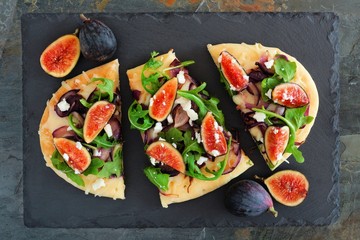 Wall Mural - Autumn flat bread pizza with figs, arugula, and goat cheese, overhead scene on slate background
