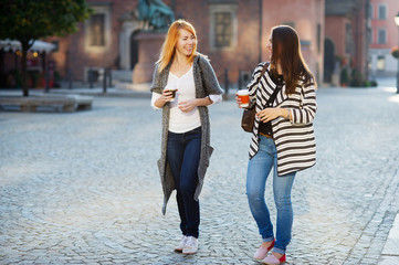 Wall Mural - Two attractive girls tourists walk the streets of the old town with a coffee in hand.