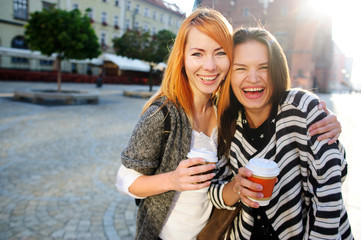 Wall Mural - Two cute young women standing on the square of the beautiful European city.