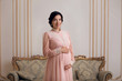 Beautiful pregnant woman in vintage dress posing for photographer. Gentle pretty woman smiling for camera in classic interior.