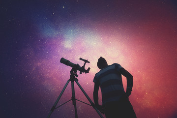 man looking at the stars with telescope beside him.
