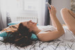 © ADDICTIVE STOCK - Smiling young woman using a  smartphone while lying on bed